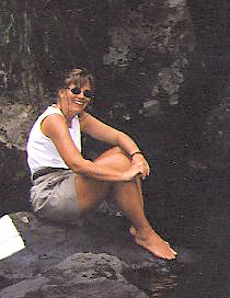 woman in bare feet sitting on a rock by a waterfall