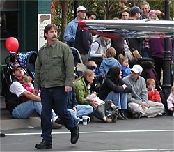 man walking next to airplane wing, with parade crowd in the background