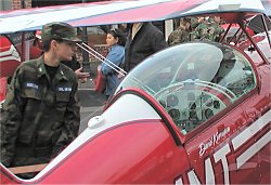 teen boy in camouflage looking into the cockpit of a small red plane