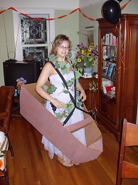 woman in dress and grape vine wearing suspenders and a cardboard boat