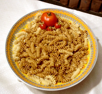 a yellow dish with spiral pasta and several tomatoes